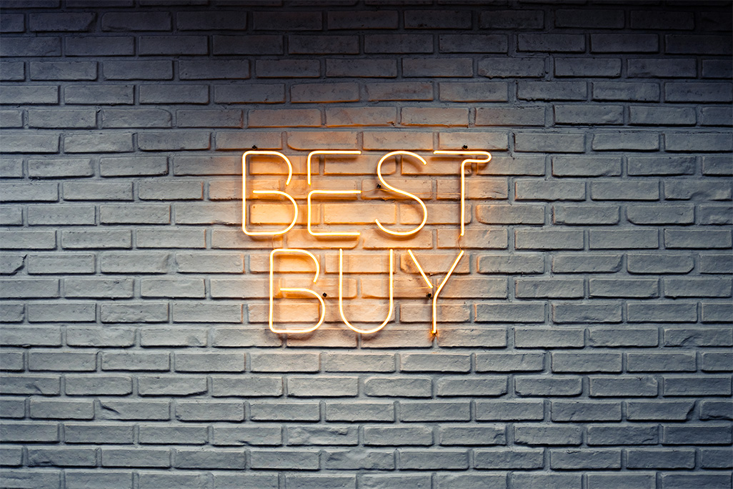 A Yellow Neon sign that reads "Best Buy." It is mounted on a white brick wall.