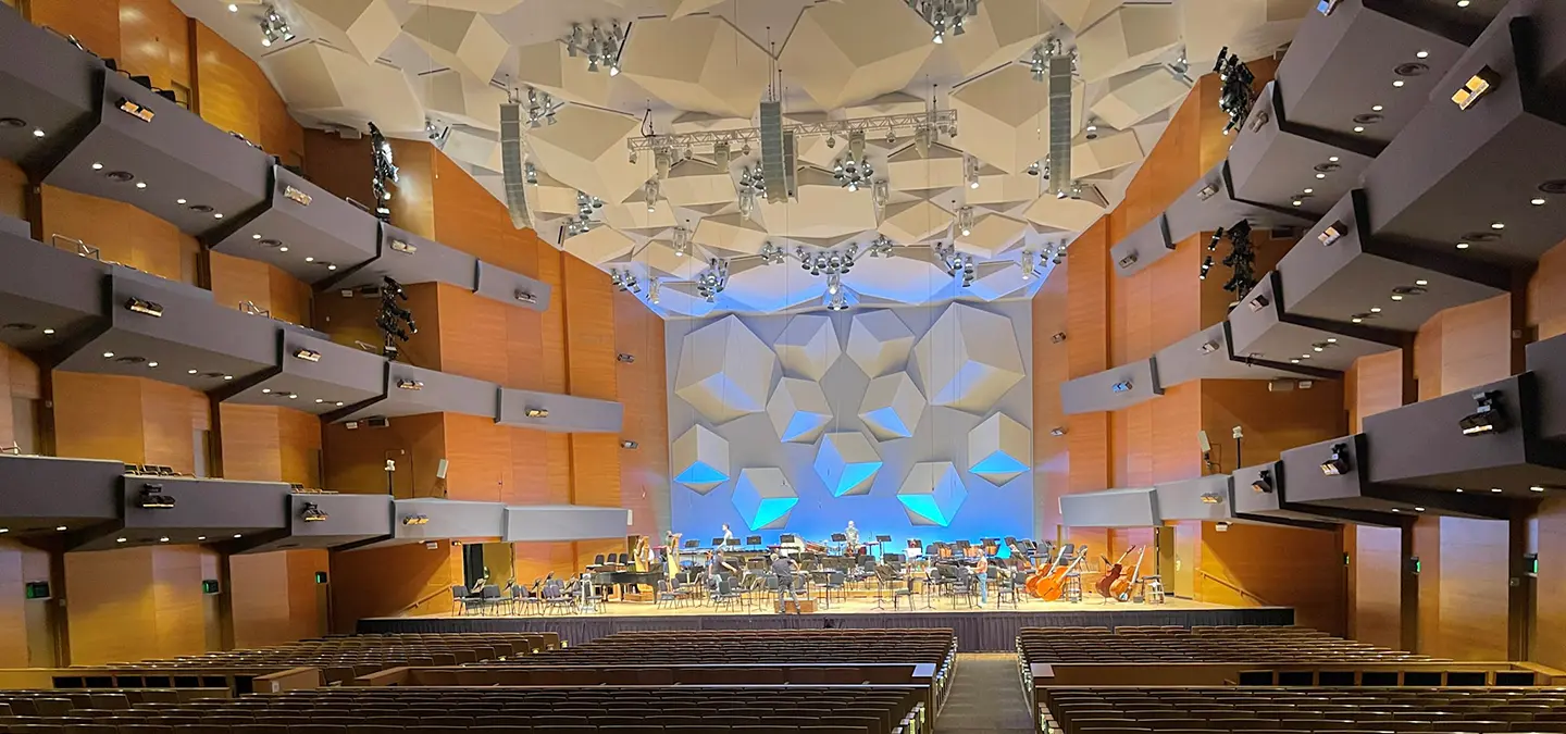 MNO_1440x675 A wide shot of the interior of the Minnesota Orchestra. A large hall is filled with chairs and upper balconys, with a large stage seen in the background of the photo.