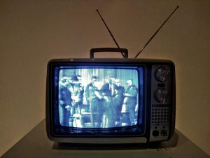 An older CRT television with an antenna. It's showing a group of people on the screen.