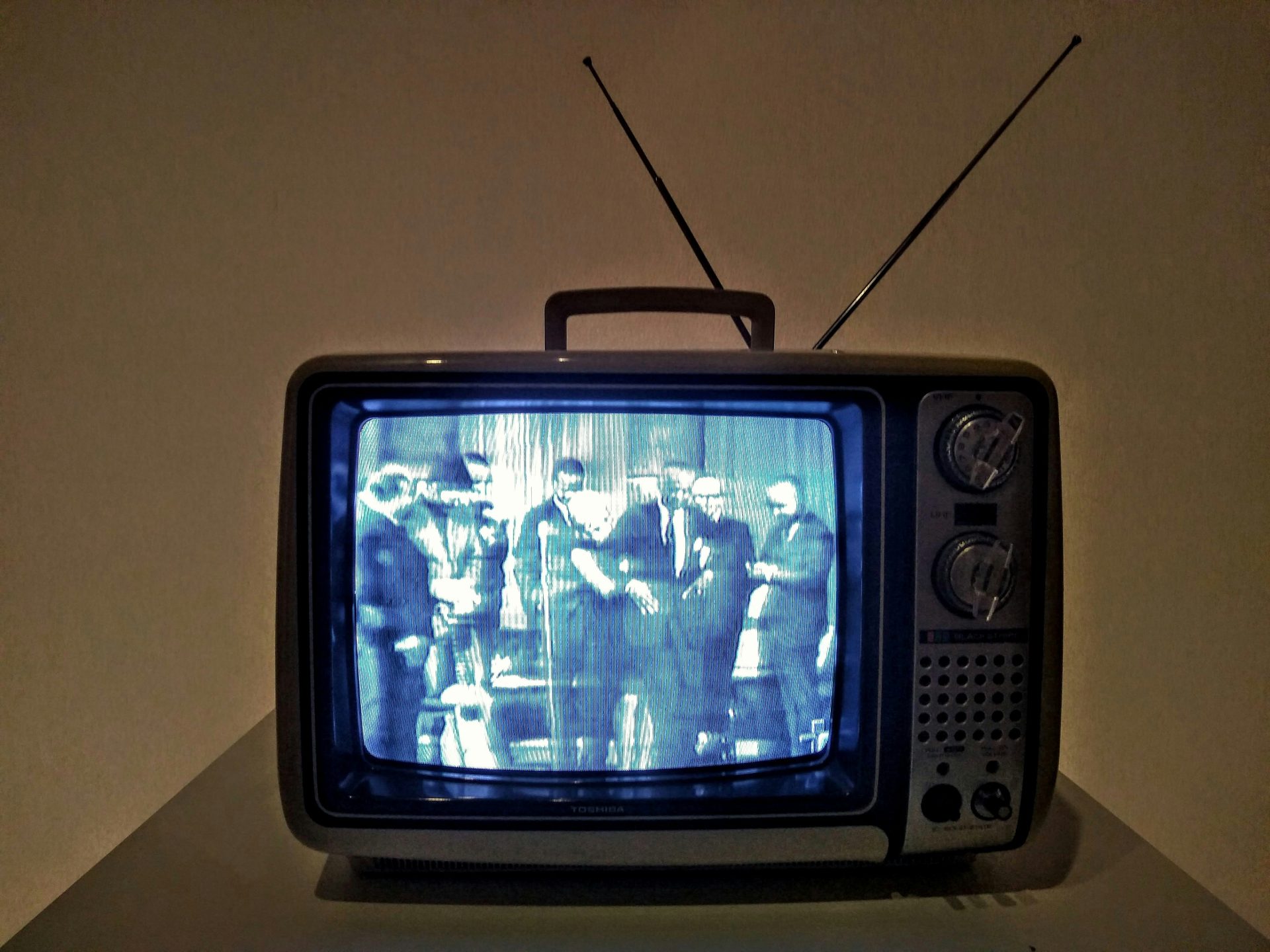 An older CRT television with an antenna. It's showing a group of people on the screen.