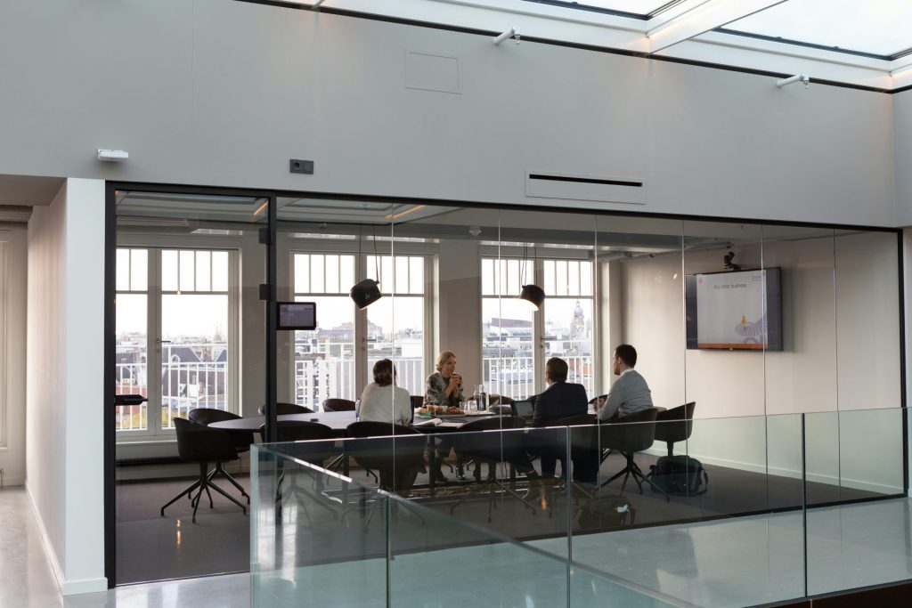 A wide shot of a meeting room. It's seen from the outside, looking into the participants through the glass walls.